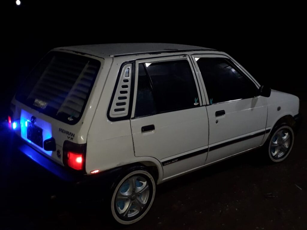 A white Suzuki Mehran car with blue lights.