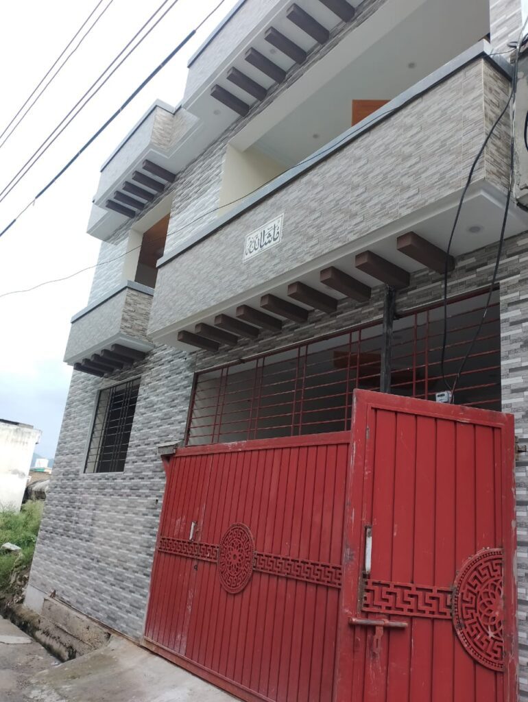 A house with a red gate and door is available for sale in Abbottabad, Pakistan.